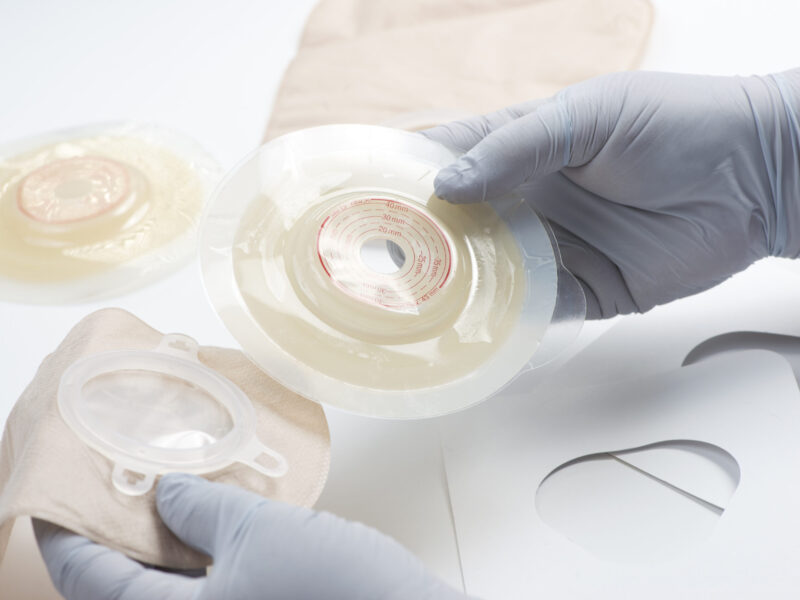 A close up of a clinician wearing gloves holding stoma appliances.