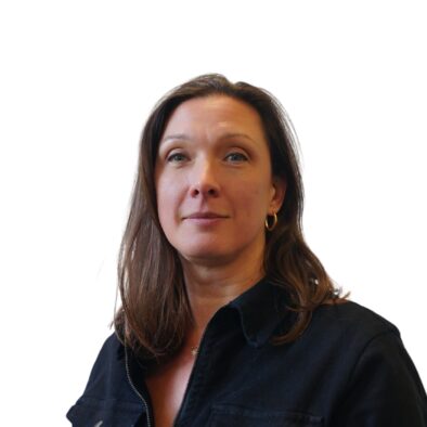 A portrait photo of Rachel Alwin - dark straight/wavy hair, slightly longer than shoulder length, blue eyes - is smiling at the camera. She is wearing a gold necklace and a black jacket in view.