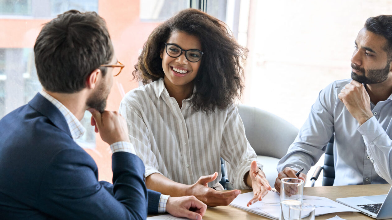 Two businessmen and a business woman sit around a table having a discussion.