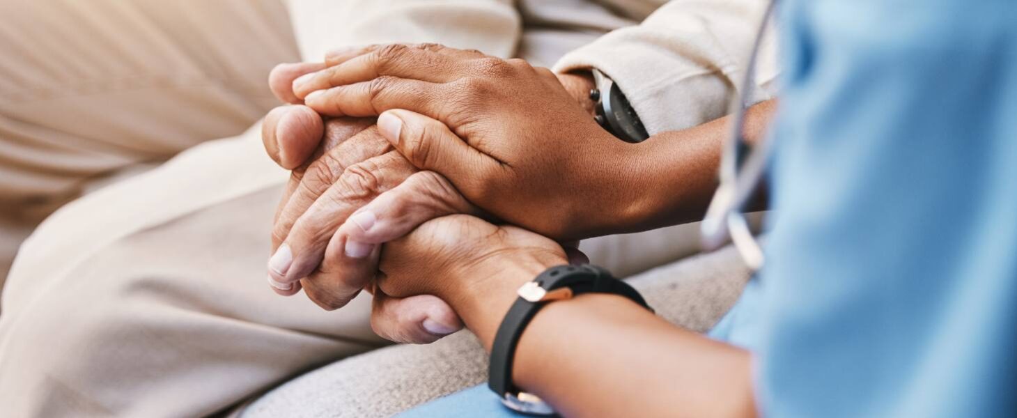 Close up of a doctor kneeling down next to a patient and holding their hands.